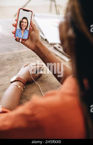 Woman taking a video call while sitting in her home office. Young graphic designer using a smartphone to attend a virtual meeting at her desk. Female Stock Photo