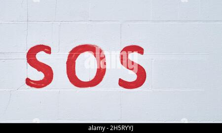 Image of the universal relief word sos painted in red on a white wall. help and assistance concept Stock Photo