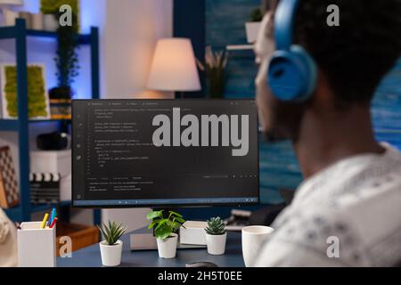 African american young developer wearing headset while typing security codes for business website working rmeote from home. Employee programming software application. Software on screen Stock Photo