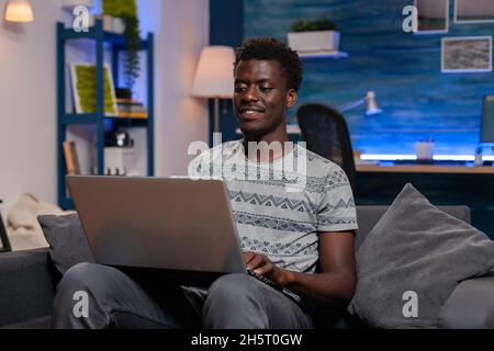 African american employee sitting on couch browsing communication information working remote from home at virtual project. Black young entrepreneur analyzing financial graph on laptop Stock Photo