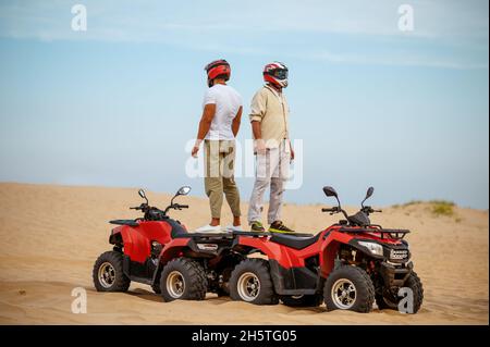 Two racers in helmets stand back to back on atvs Stock Photo