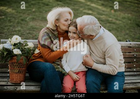 Heathy senior couple sitting on the bench witht heir cute little granddaughter Stock Photo