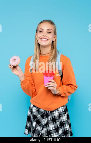 Cheerful student with backpack holding paper cup and donut isolated on blue Stock Photo