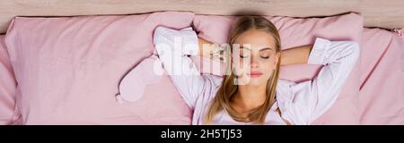 Top view of young woman in pajamas lying near mask on bed, banner Stock Photo