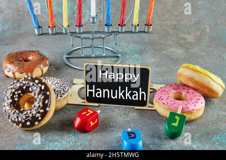 Happy Hanukkah and Hanukkah Sameach - traditional Jewish candlestick with candles, donuts and spinning tops with the inscription Happy Hanukkah. Stock Photo