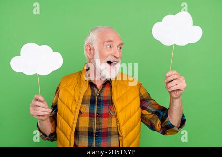 Photo of pretty excited senior gentleman wear yellow vest holding looking empty space clouds smiling isolated green color background Stock Photo