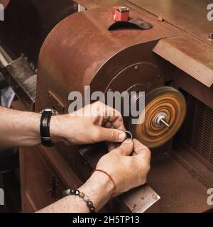 A worker in a jewelry workshop polishes a gold ring on a special machine Stock Photo