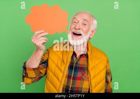 Photo of excited funky senior gentleman wear yellow vest holding empty space talking cloud smiling isolated green color background Stock Photo