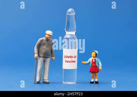 Little toy men made of plastic and an ampoule with a vaccine on a blue background, the concept of the need for vaccination against coronavirus Stock Photo
