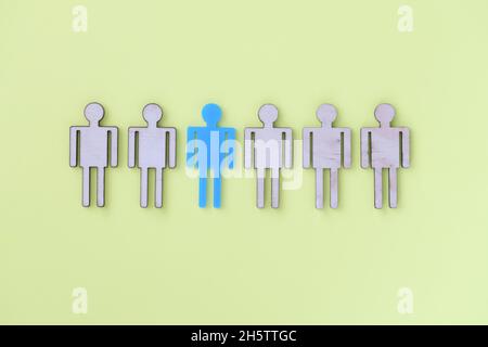 Figures of beige wooden little men in middle one blu Stock Photo