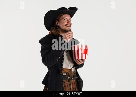 Cropped portrait of brutal smiling man, pirate in vintage costume eating popcorn isolated over white background Stock Photo