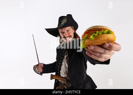 Cropped portrait of brutal man, pirate in vintage costume with sword proposing burger isolated over white background Stock Photo