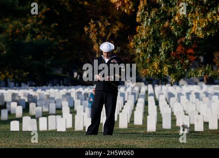 Arlington, USA. 11th Nov, 2021. A United States sailor holds onto an American flag amid graves on Veterans Day in Arlington National Cemetery in Arlington, Virginia, U.S., November 11, 2021. Credit: Jonathan Ernst/Pool via CNP /MediaPunch Credit: MediaPunch Inc/Alamy Live News Stock Photo