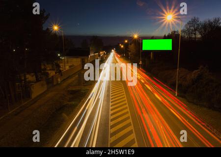 Long exposure car light trail on asphalt road with green screen billboard for advertisment placement. Traffic concept, Ceske Budejovice, Czech republi Stock Photo