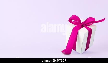 White gift box with red ribbon over purple background. With space for your Christmas, birthday or Valentines day greetings Stock Photo
