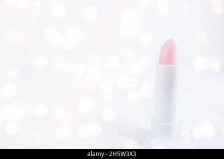 A white tube of pink lipstick balm to protect and nourish lips. Winter season cosmetics. Mock up container in the snow. Christmas present for women id Stock Photo