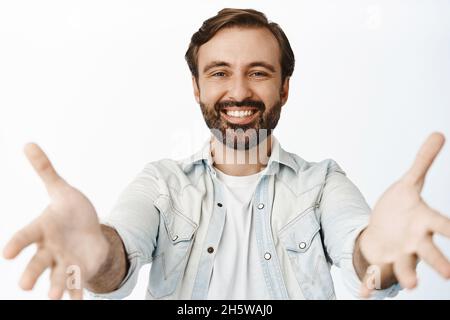 Portrait of happy smiling man with beard, stretching out hands, reaching for hug, hold something in his arms, white background Stock Photo