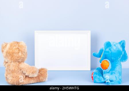 Toys with empty white frame on light blue background. Toy teddy bear, plush stuffed elephant and white wooden picture frame with blank mock up copy Stock Photo
