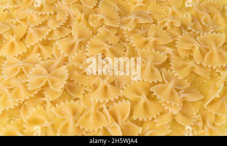 Uncooked dried bow-tie pasta as yellow culinary background. Closeup of raw egg farfalle of wheat flour dough beautiful texture. Butterfly pastas heap. Stock Photo