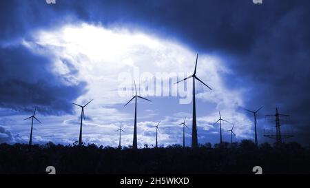windmills producing electricity silhouetted in a dark blue sky Stock Photo