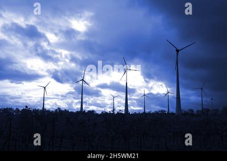 windmills producing electricity silhouetted in a dark blue sky Stock Photo
