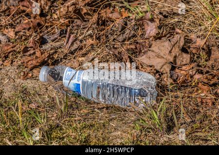 Unopened plastic bottle of water laying on the ground alongside the trail in the park discarded or dropped polluting the environment Stock Photo