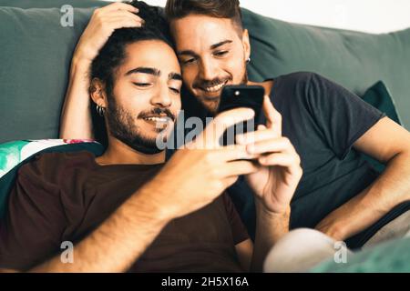 Male gay couple using smartphone in the bedroom - homosexual LGBT concept - focus on the left man Stock Photo