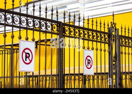 No Parking Sign on black metal wrought iron fence against yellow brick wall. Private territory exterior, property, house protection. Decorative cast i Stock Photo