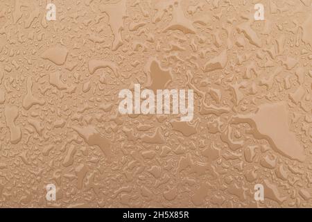 Irregular patterned water drops on a beige, sand-coloured shiny metal surface Stock Photo