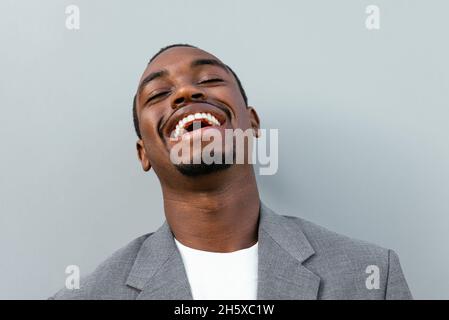 Happy African American male entrepreneur in formal suit laughing while standing against gray background Stock Photo