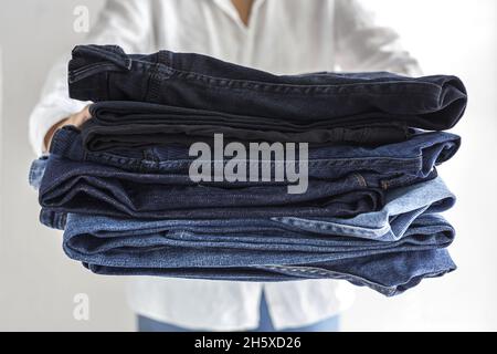 Crop anonymous female in white shirt with stack of blue jeans in hands Stock Photo