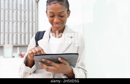Concentrated African American female student with short hair and backpack surfing tablet while standing on white background Stock Photo