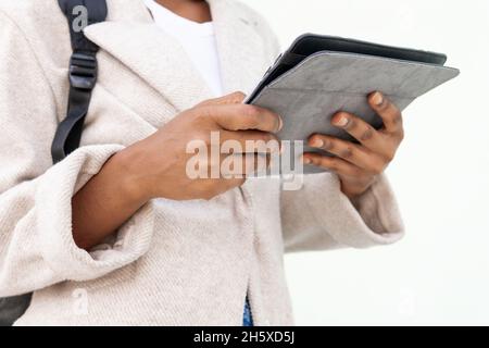 Side view of anonymous African American female student with backpack surfing tablet while standing on white background Stock Photo