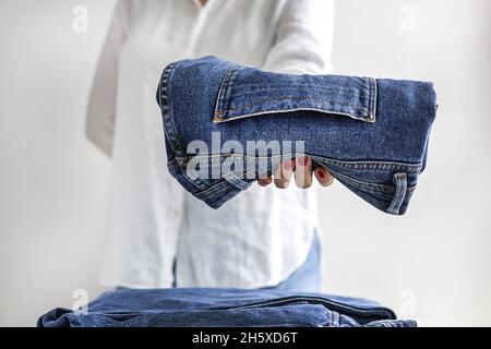 Crop anonymous female in white shirt with stack of blue jeans in hands Stock Photo