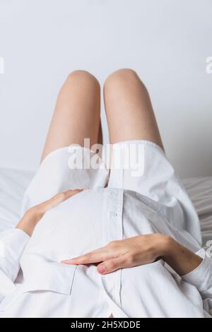 From above anonymous young gentle pregnant female touching tummy while lying down on bed Stock Photo