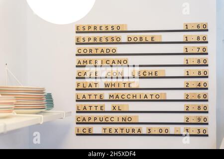 Menu board with various coffee drinks and prices on white wall near counter with dishware in modern light coffee house with glowing light Stock Photo