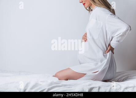 Side view of anonymous young pregnant gentle female touching tummy while sitting on bed Stock Photo