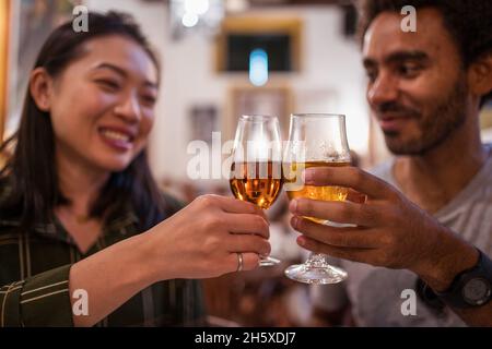 Soft focus of multiracial couple clinking glasses of alcohol drinks while having dinner together in modern restaurant during festive event Stock Photo