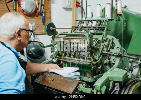 Crop faceless middle aged male worker putting pile of papers into aged metal cutting machine in factory Stock Photo