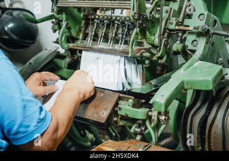 Crop faceless middle aged male worker putting pile of papers into aged metal cutting machine in factory Stock Photo