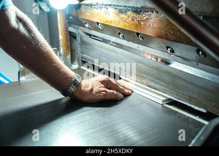 Crop unrecognizable aged male artisan putting paper sheets into metal printing machine with glowing lamp in factory Stock Photo
