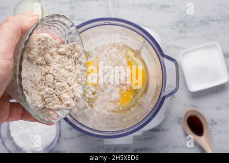 Top view of crop anonymous male pouring healthy almond flour into blender with eggs while cooking keto crepes in kitchen Stock Photo