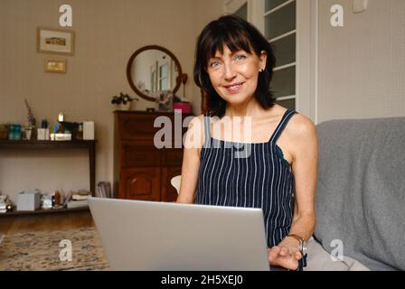 Happy female sitting on couch working on laptop at home Stock Photo