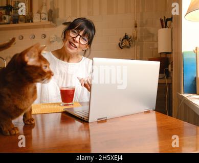 Attractive young hipster in snapback and eyeglasses sitting and holding gaming controller on red background Stock Photo