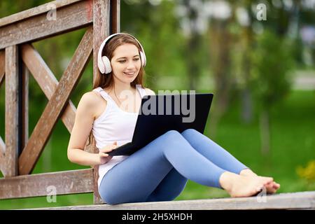 Online learning or teleworking using laptop connected internet via 5g network, young woman does e-learning while visiting public park. Stock Photo