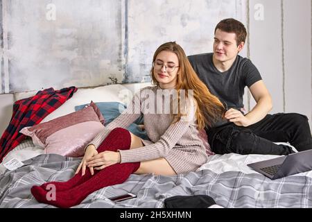 Young couple is sitting on bed, guy is combing his girlfriend. Stock Photo