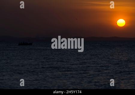 Salvador, Bahia, Brazil - October 29, 2015: Sunset seen from Ribeira beach in Salvador, Bahia, Brazil. A boat sails at sea. Stock Photo