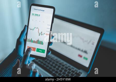 Trader using stock exchange app online for trading operations in mobile phone - Focus on left hand holding smartphone Stock Photo