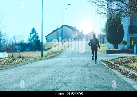 unrecognizable woman trains by running the streets of the town, the weather is cold but she faces reality and keeps fit anyway Stock Photo