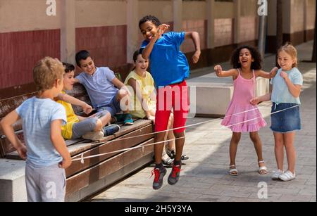 Energetic kids playing and skipping on elastic jumping rope in yard Stock Photo